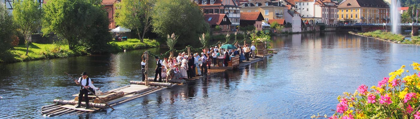 Murgfloß beim Altstadtfest Das Murgfloß mit den Flößern, Biedermeiergruppe in Kostümen und Gästen vor der Altstadtkulisse in der Murg