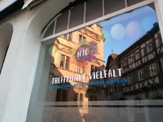 Das Schaufenster mit der Beklebung H10 - Treffpunkt Vielfalt, darin spiegelt sich das Alte Rathaus