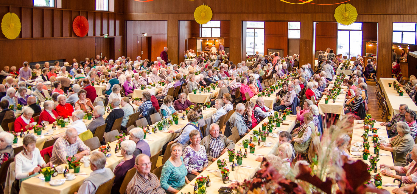 Gäste beim Seniorennachmittag in der Stadthalle sitzen an gedeckten Tischen