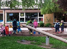 Kinder spielen im Sandkasten neben einer Wippe.