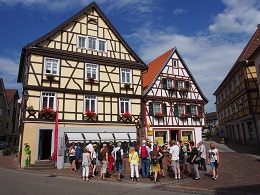 Gruppe bei einer Führung beim Brunnen vor zwei Fachwerkhäusern an der Hofstätte